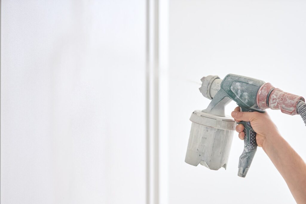 Worker painting wall with spray gun in white color.